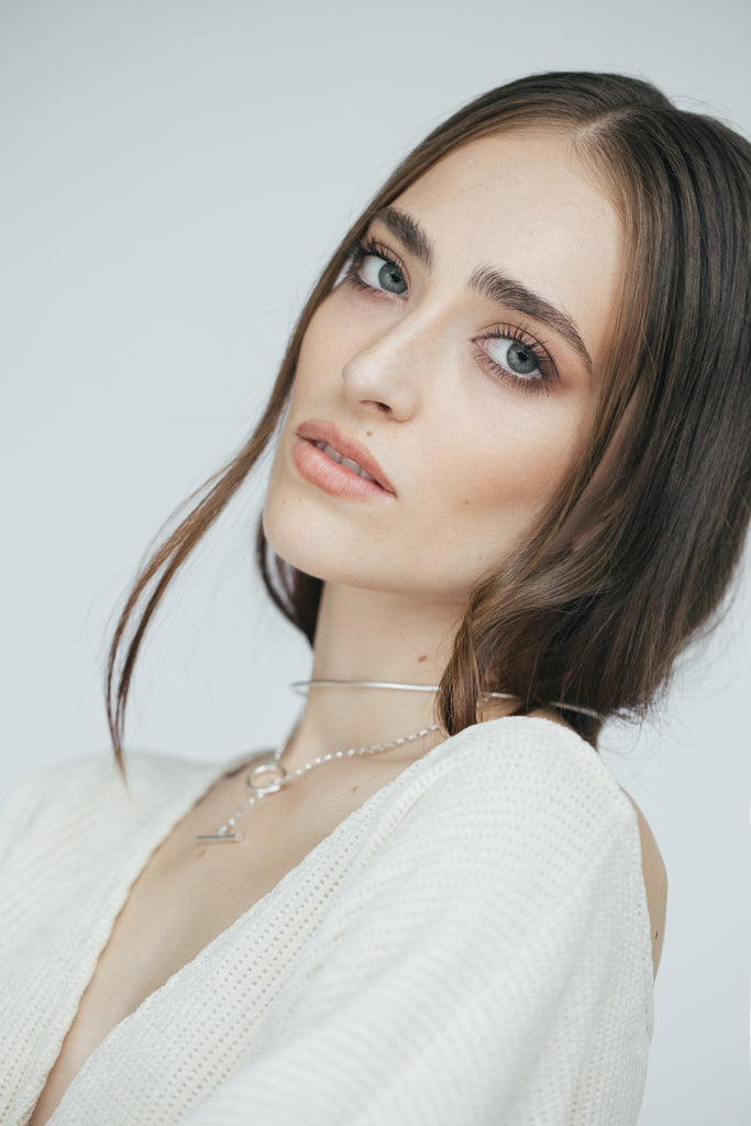 Model wearing two minimalist silver necklaces: one rigid chocker necklace and one chain necklace.
