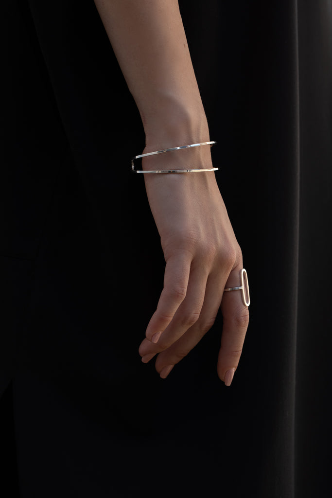 Model wearing contemporary silver bangle and silver ring with front large oval piece.