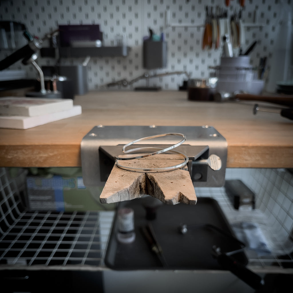 Silver bracelet standing on a jewelry bench peg. 